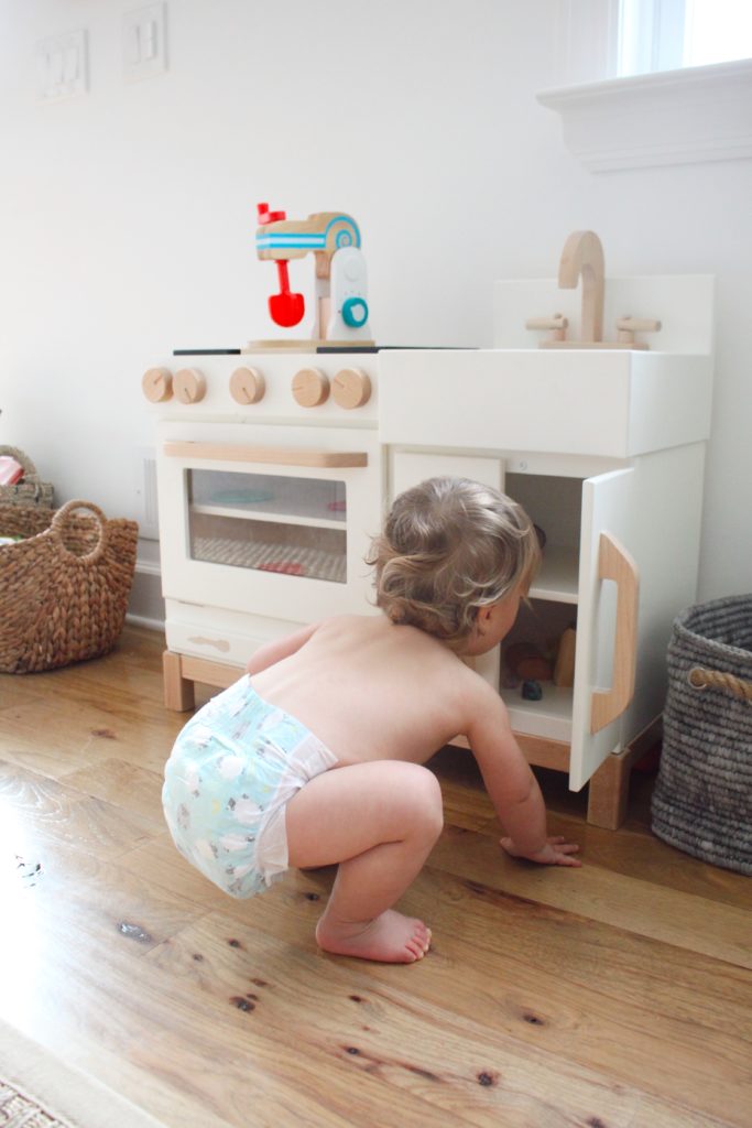toddler in diaper near wooden pretend play kitchen